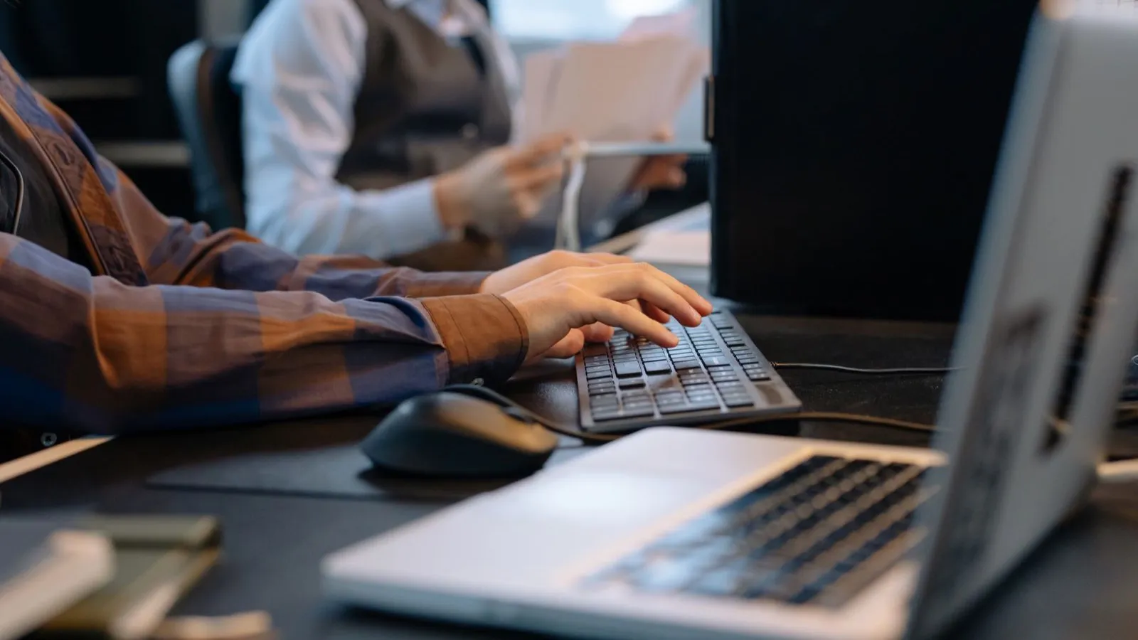 Administratívny pracovník píše na klávesnici, kolegyňa v pozadí triedi papiere