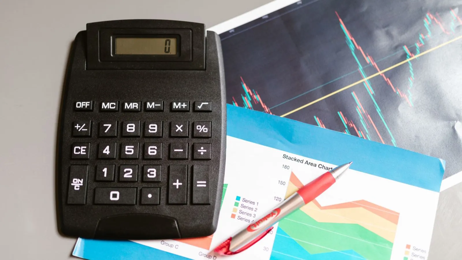 Kalkulačka položená na vytlačených finančných grafoch vedľa pera