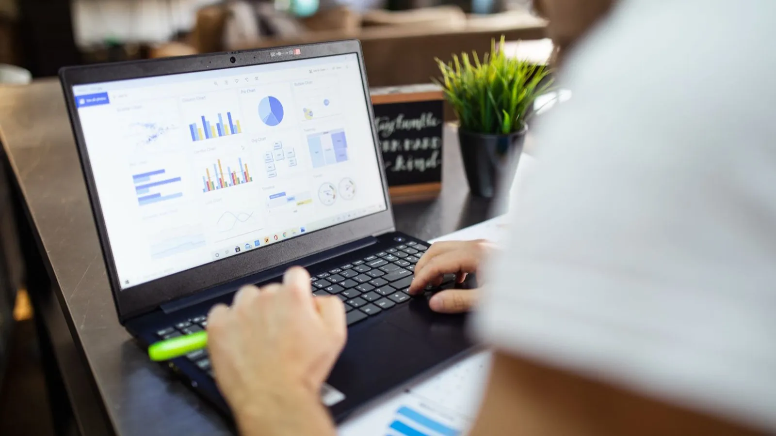 Človek si na notebooku prezerá tabuľkový dashboard so stĺpcovými a koláčovými grafmi